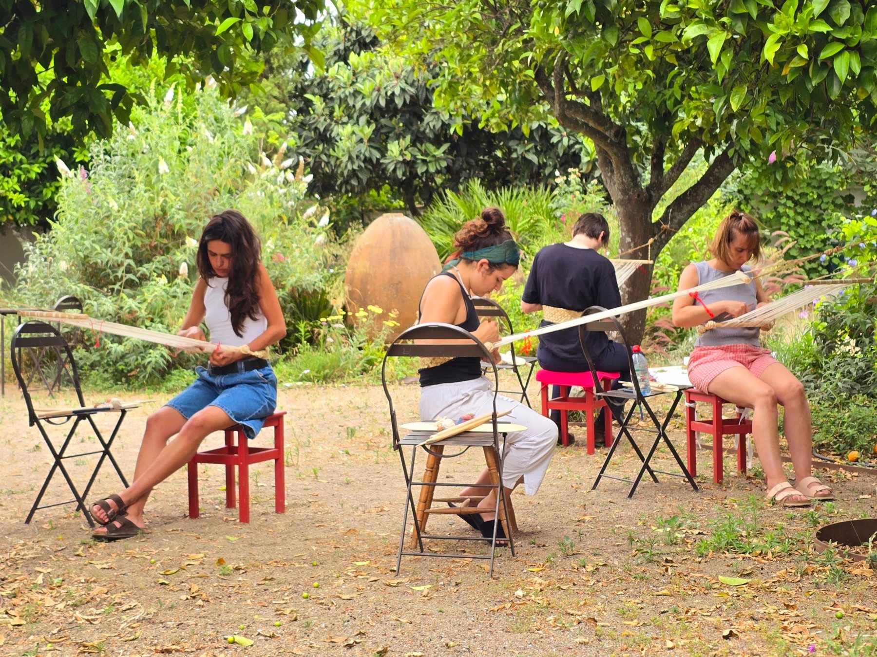 Artists weaving with backstrap looms in the garden